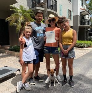 A joyous family proudly displaying their Ora Dog Training certificate alongside their beloved dog, celebrating shared achievements in South Florida.
